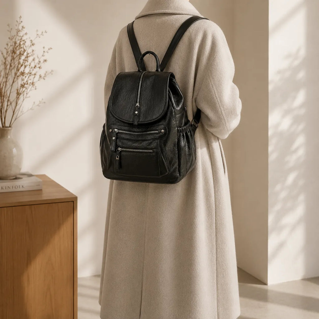 Sac a dos femme noir style cuir porte avec manteau long beige dans un interieur minimaliste