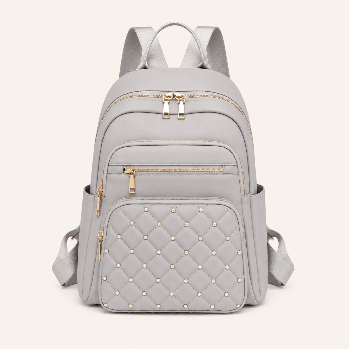 Sac à dos femme gris clair matelassé avec détails dorés et poches zippées vu de face