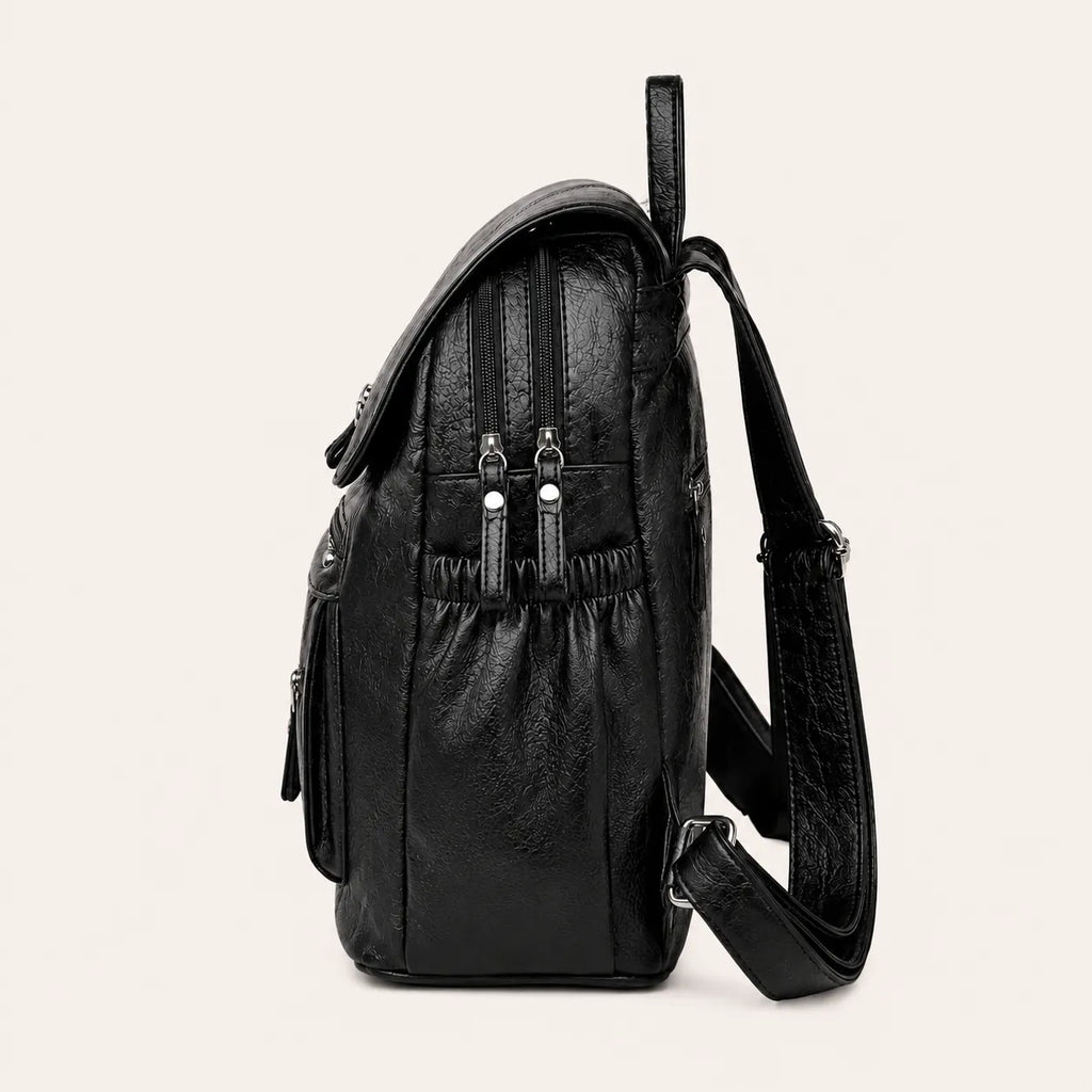 Vue latérale d’un sac à dos femme noir effet cuir avec poches zippées et bandoulière réglable sur fond beige #F6F0ED