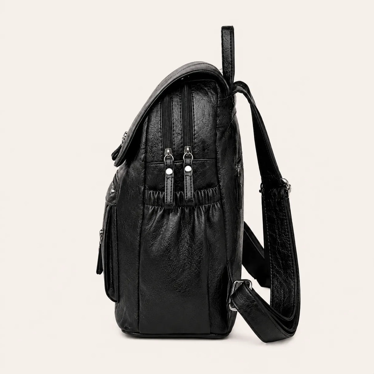 Vue latérale d’un sac à dos femme noir effet cuir avec poches zippées et bandoulière réglable sur fond beige #F6F0ED