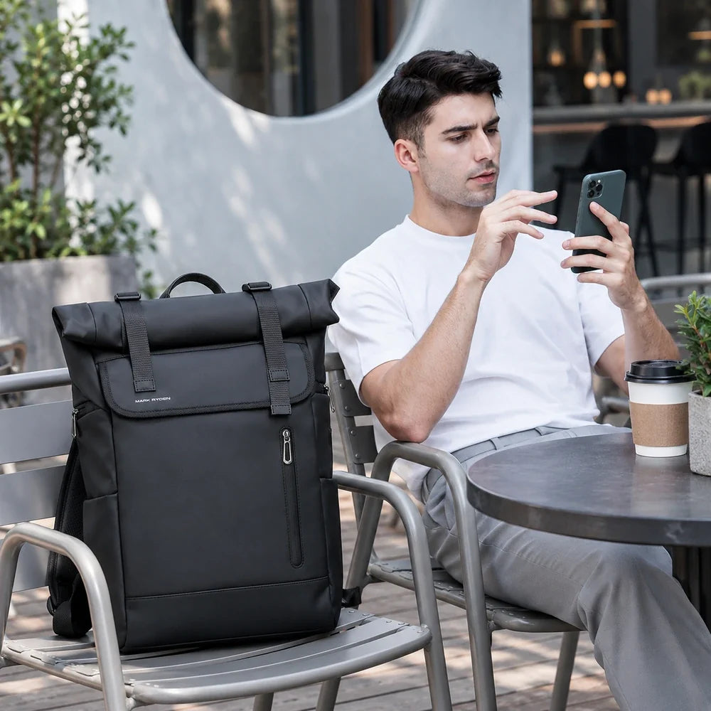 Le Nomade, sac à dos ordinateur Roll Top noir posé à côté d’un utilisateur au café