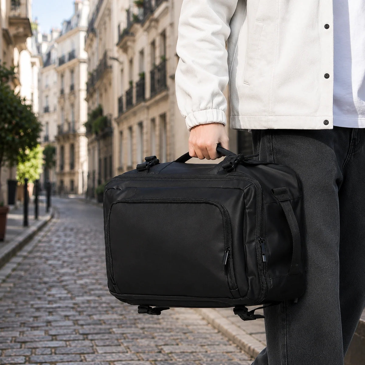 Sac ordinateur convertible Le Transit 3-en-1 noir, porté à la main par sa poignée mallette